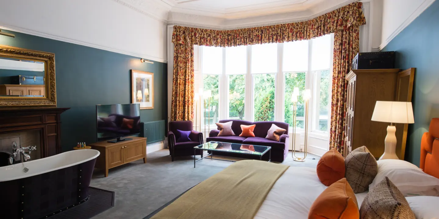 An elegantly furnished hotel room featuring a comfortable bed, plush couch, and modern television.