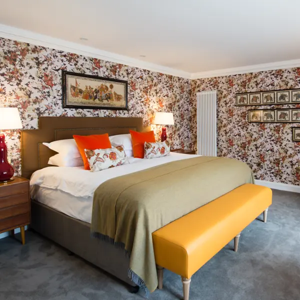 An elegantly furnished bedroom featuring a comfortable bed, a stylish chair, a sleek table, and captivating artwork adorning the walls.