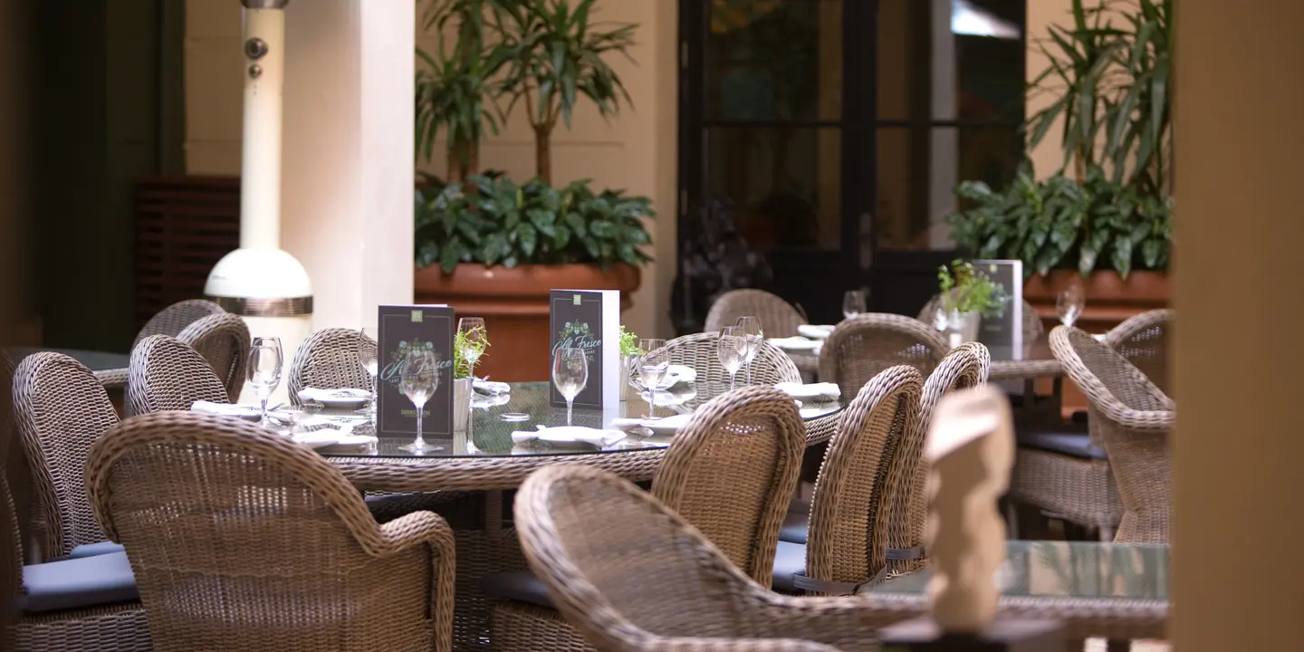 Straw dining seats surrounding dining tables which are place outside of the restaurant