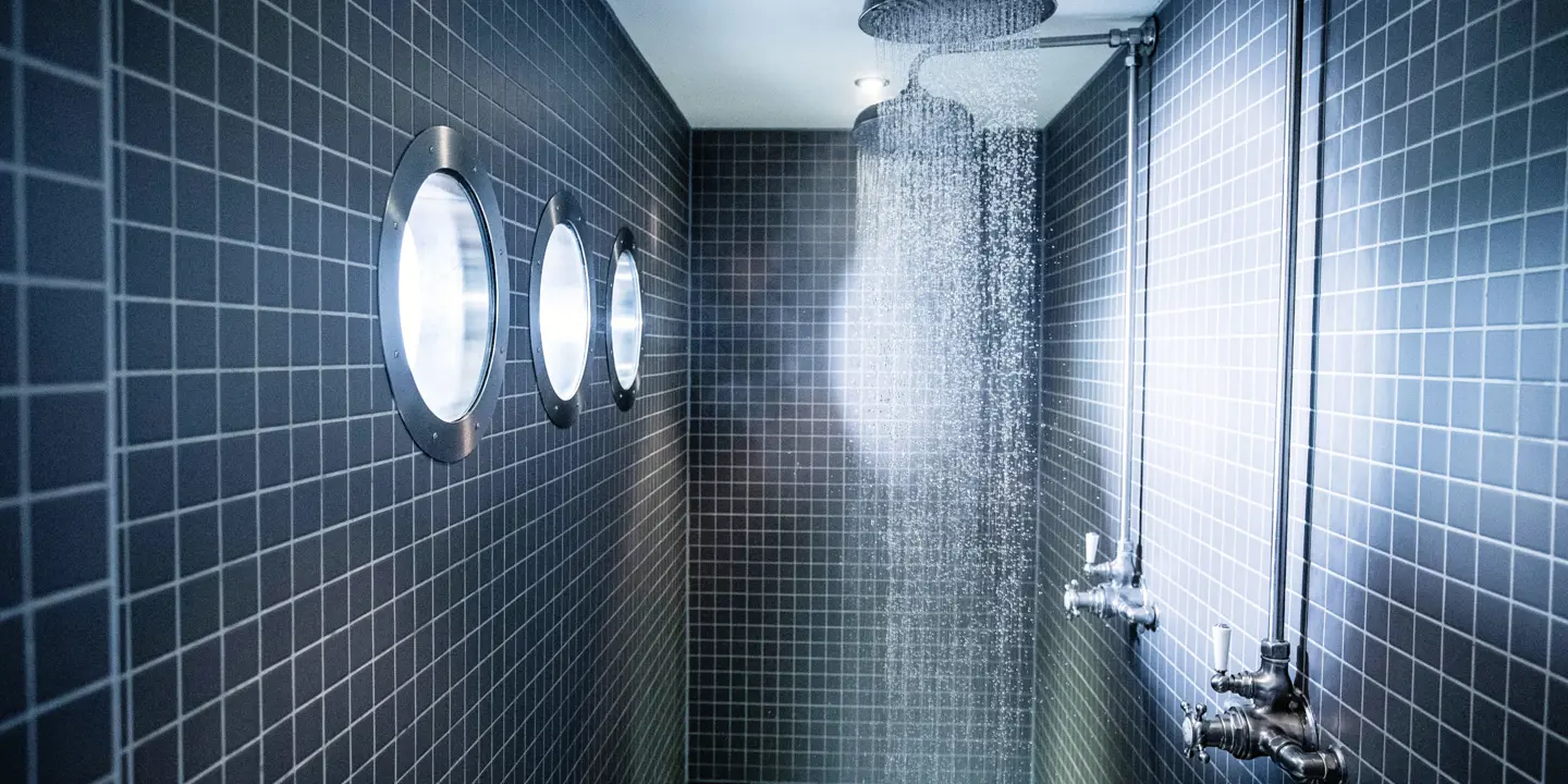 Shower head in a tiled bathroom next to a window.