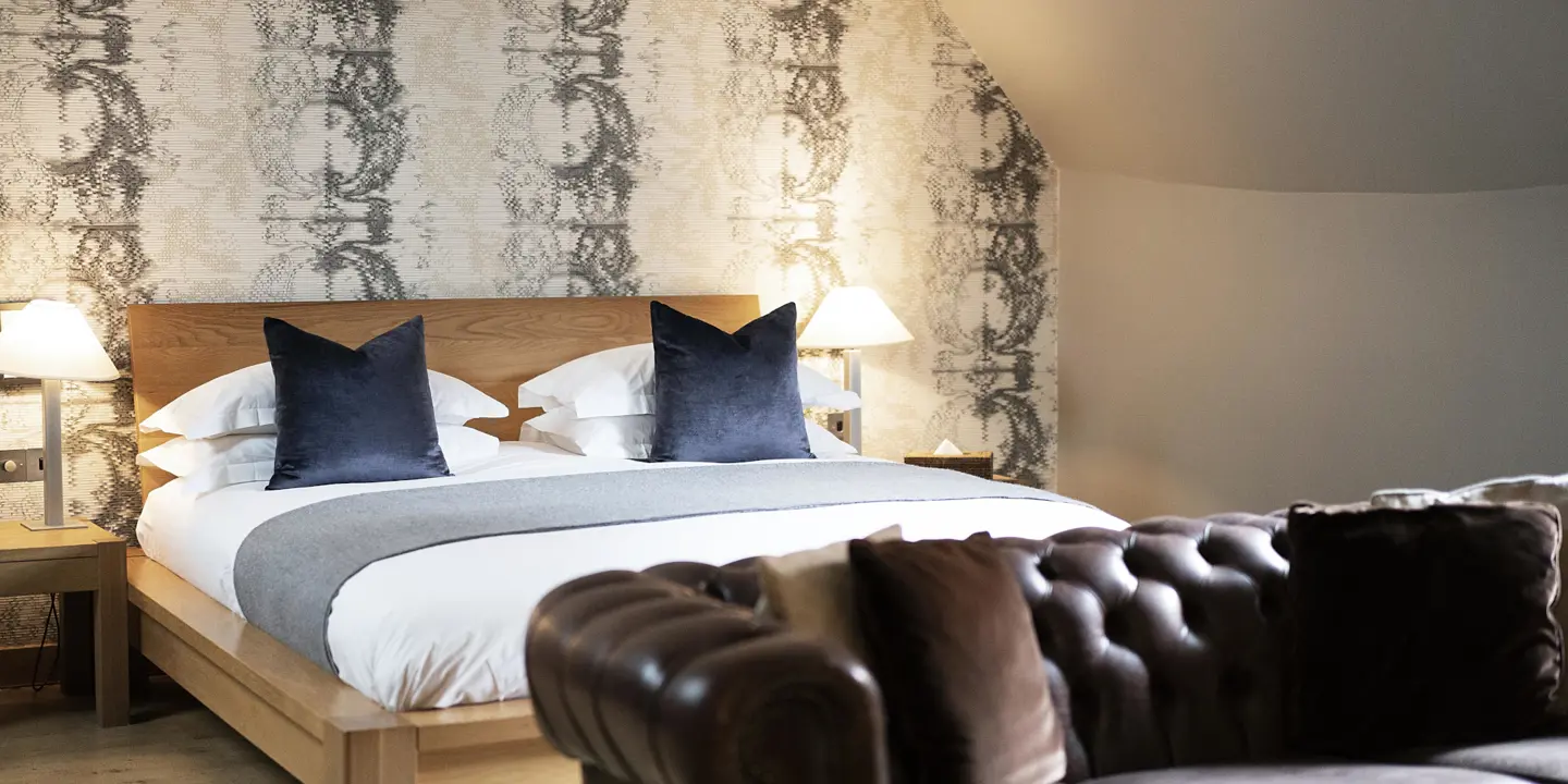 Brown leather sofa in front of a spacious light wood bed frame adorned with plump pillows