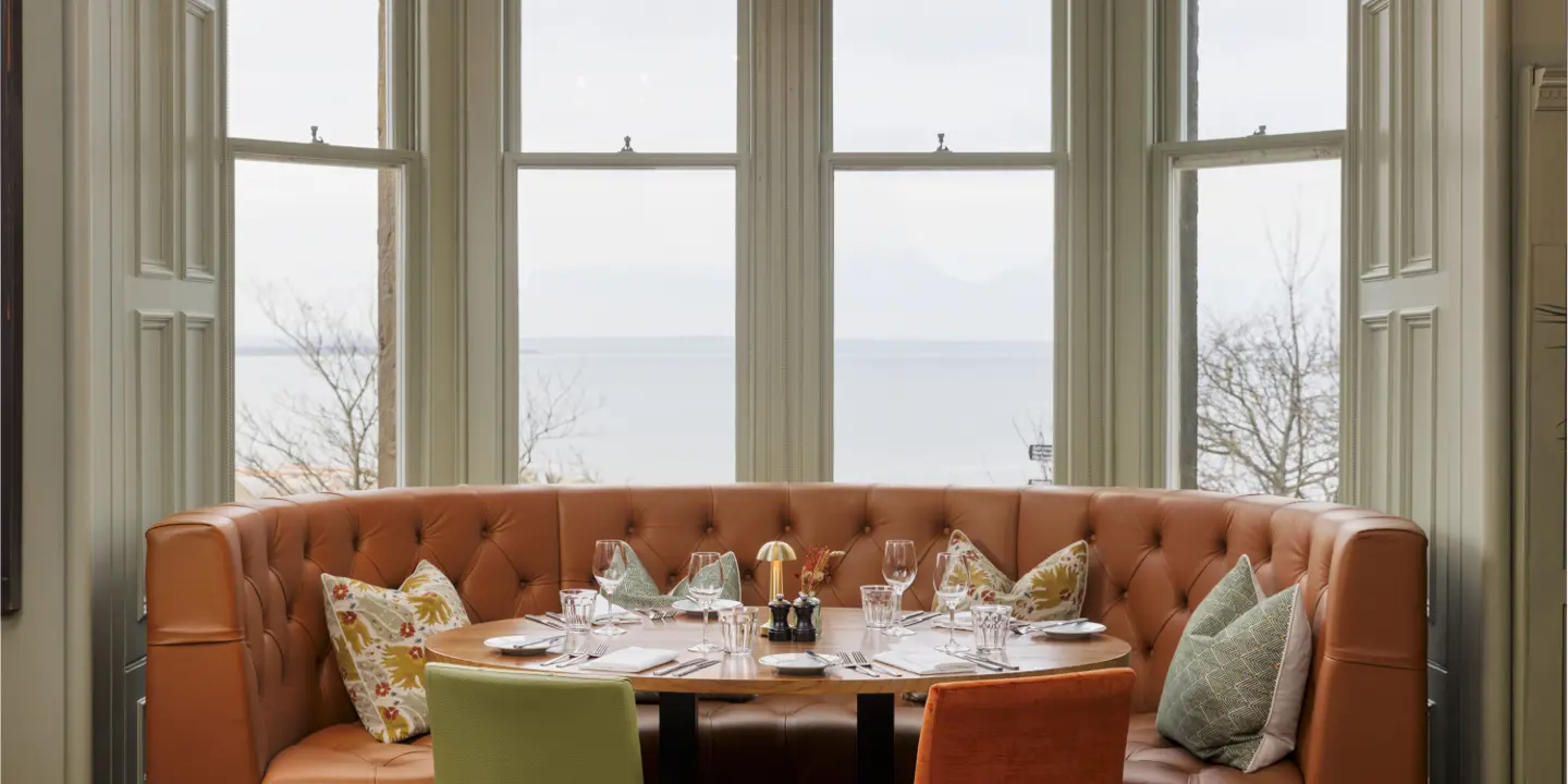 A beautifully arranged table with elegant wine glasses and neatly set place settings, placed in front of a picturesque bay window.